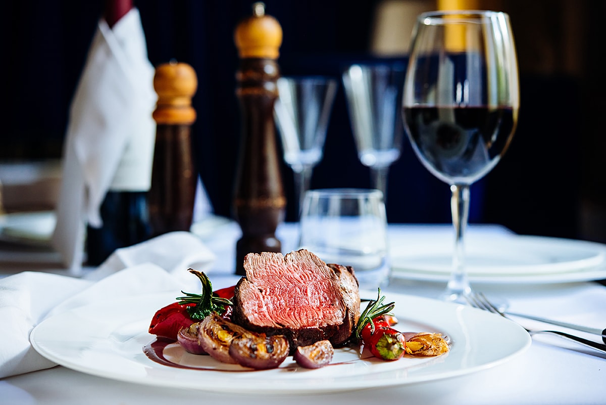 Das Foto zeigt ein perfekt arrangiertes Steak mit Gemüse auf einem Teller, begleitet von einem Rotweinglas und stilvollem Tischarrangement.