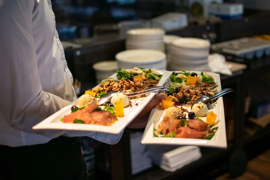 Das Foto zeigt einen Koch, der zwei reichlich bestückte Cateringplatten serviert, und veranschaulicht das Thema „Catering Dresden“.